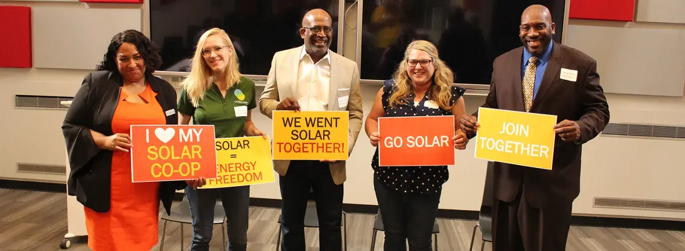 Image: people stand holding signs that say "I love my solar co-op, "Solar = Energy Freedom," "We Want Solar Together!," "Go Solar," and "Join Together." Title: Getting to 100% Clean Energy, Equitably